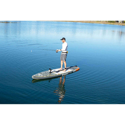 Person fishing on Solstice Watersports inflatable paddleboard in serene lake setting.