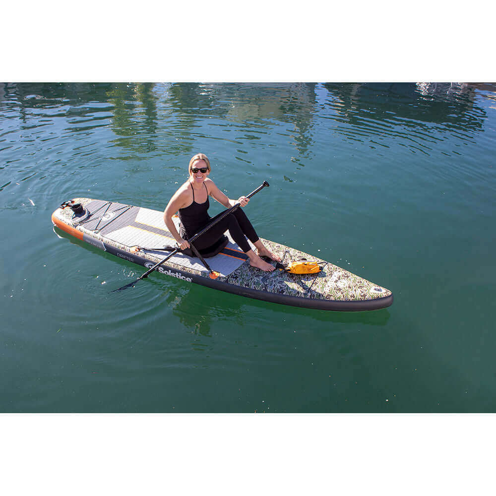 Woman on Solstice Drifter fishing paddleboard with paddle in calm water.