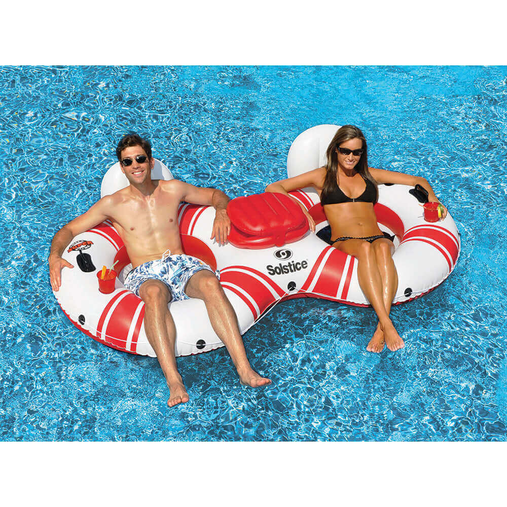 Two people relaxing on Solstice Watersports 2-Person River Tube with cooler, in a blue pool.