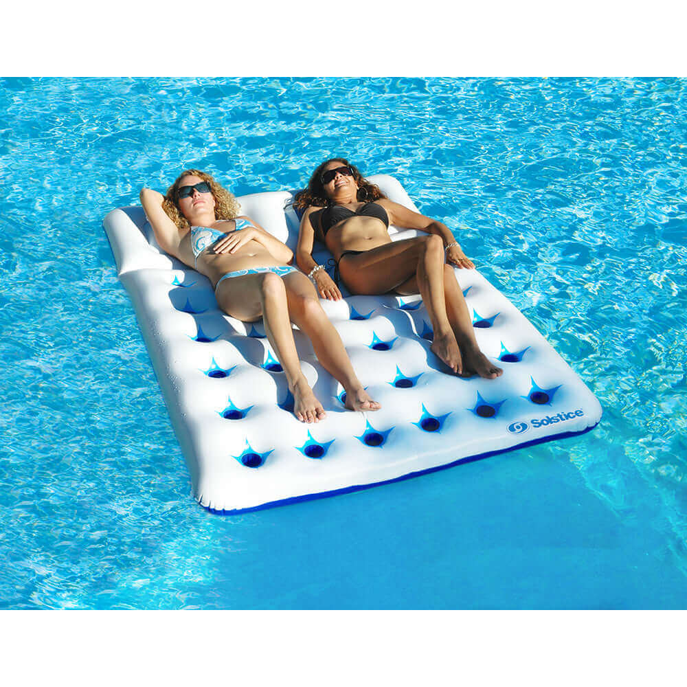 Two people relaxing on a Solstice Watersports Aqua Window Duo Floating Mattress in a pool.