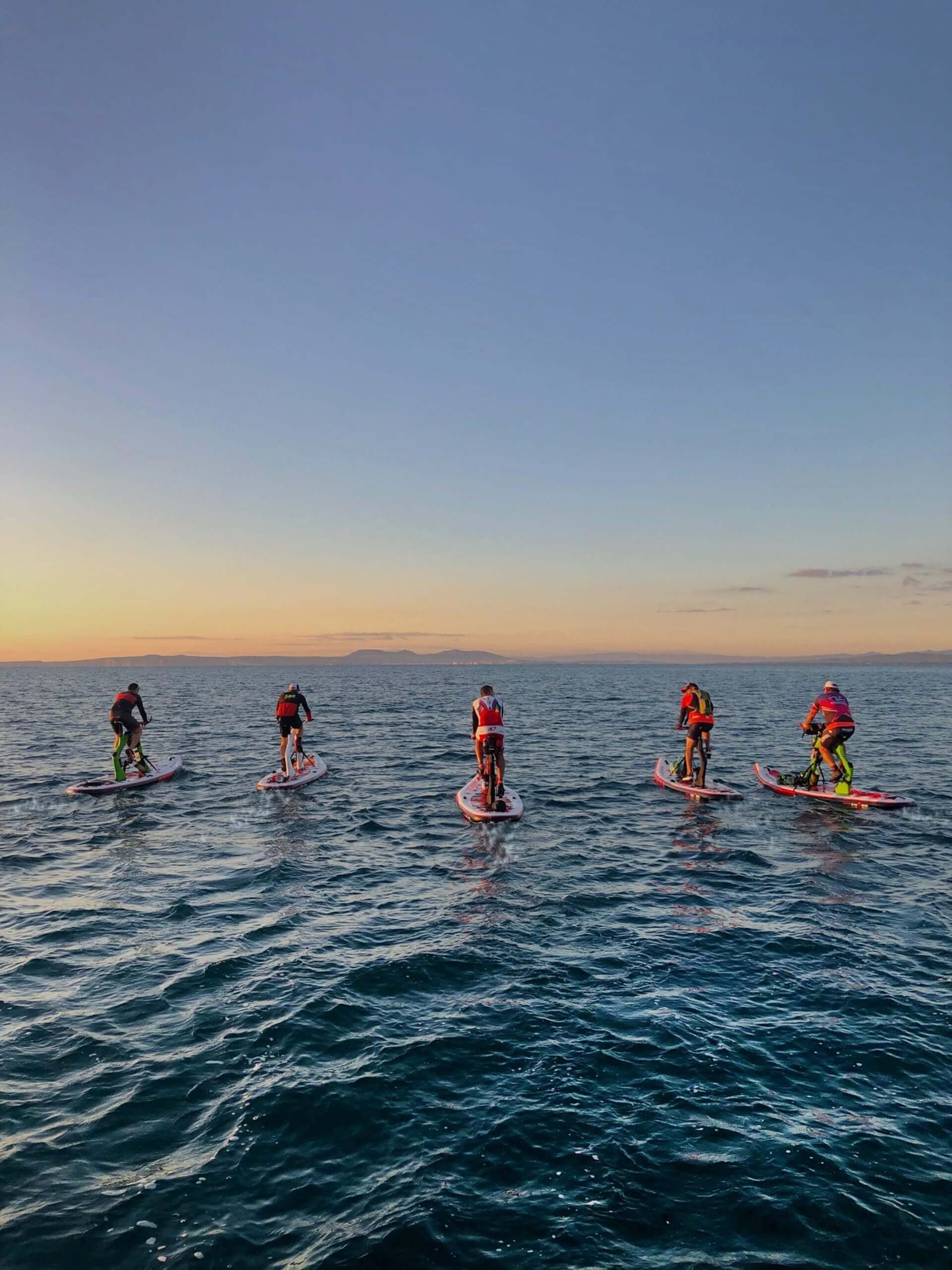 Group paddleboarding workout on open water at sunset with Red Shark Fitness equipment.