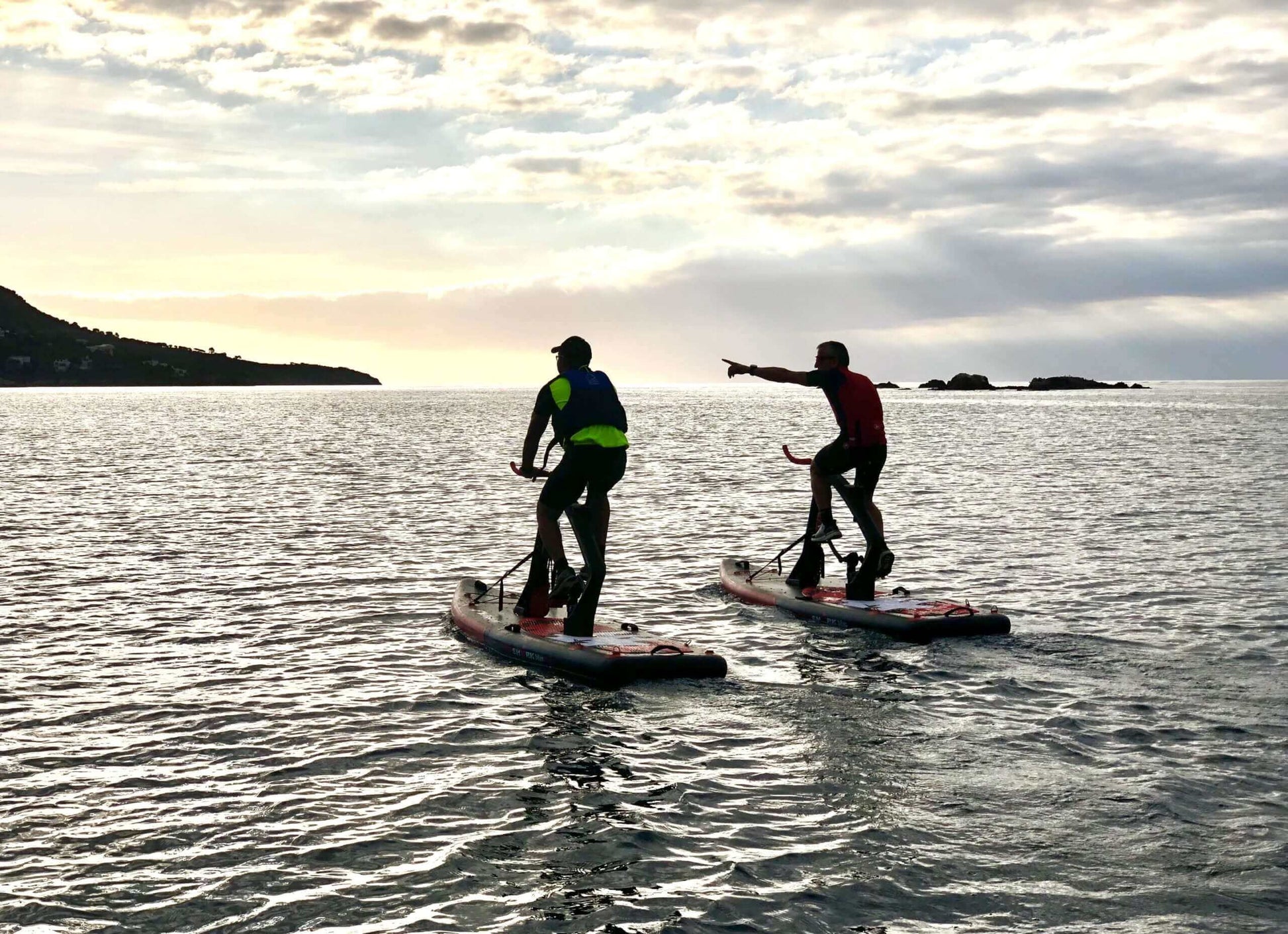 Two people enjoying a workout on Red Shark Fitness boards in the ocean at sunset.