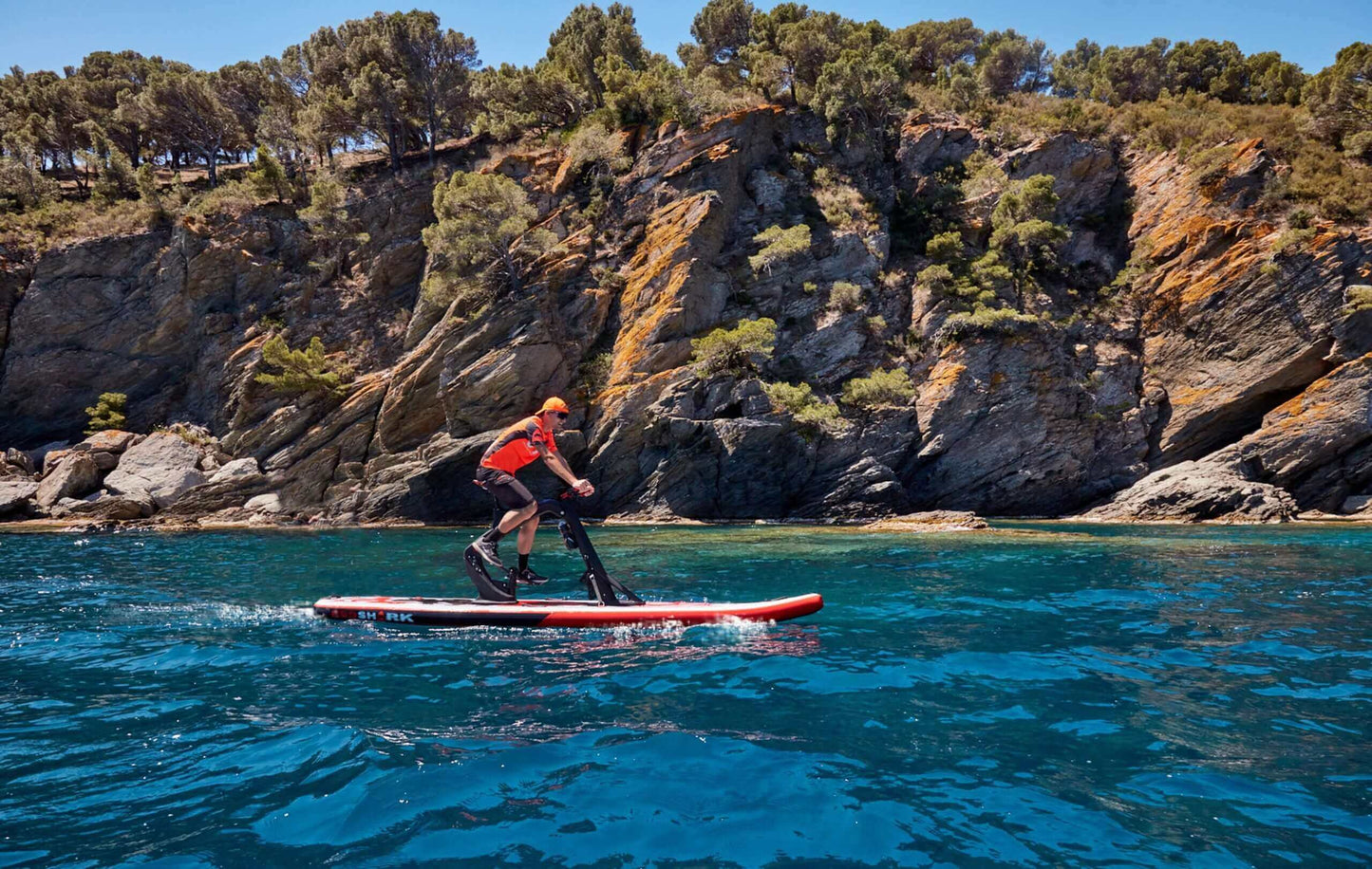 Person riding the Red Shark Fitness water bike near rocky coast, enjoying a workout in nature.