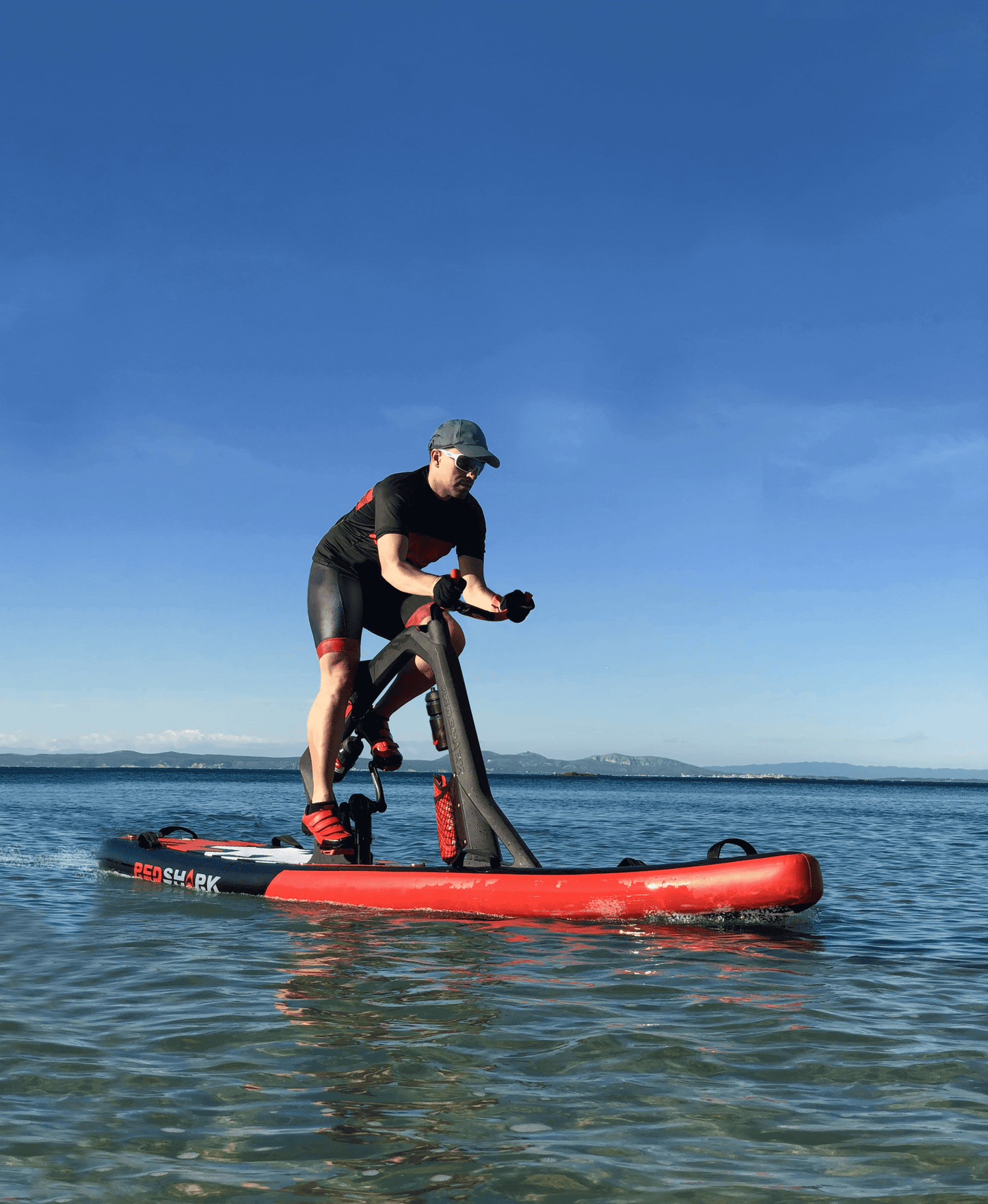 Person enjoying a workout on a Red Shark fitness board, gliding on water under a clear blue sky.