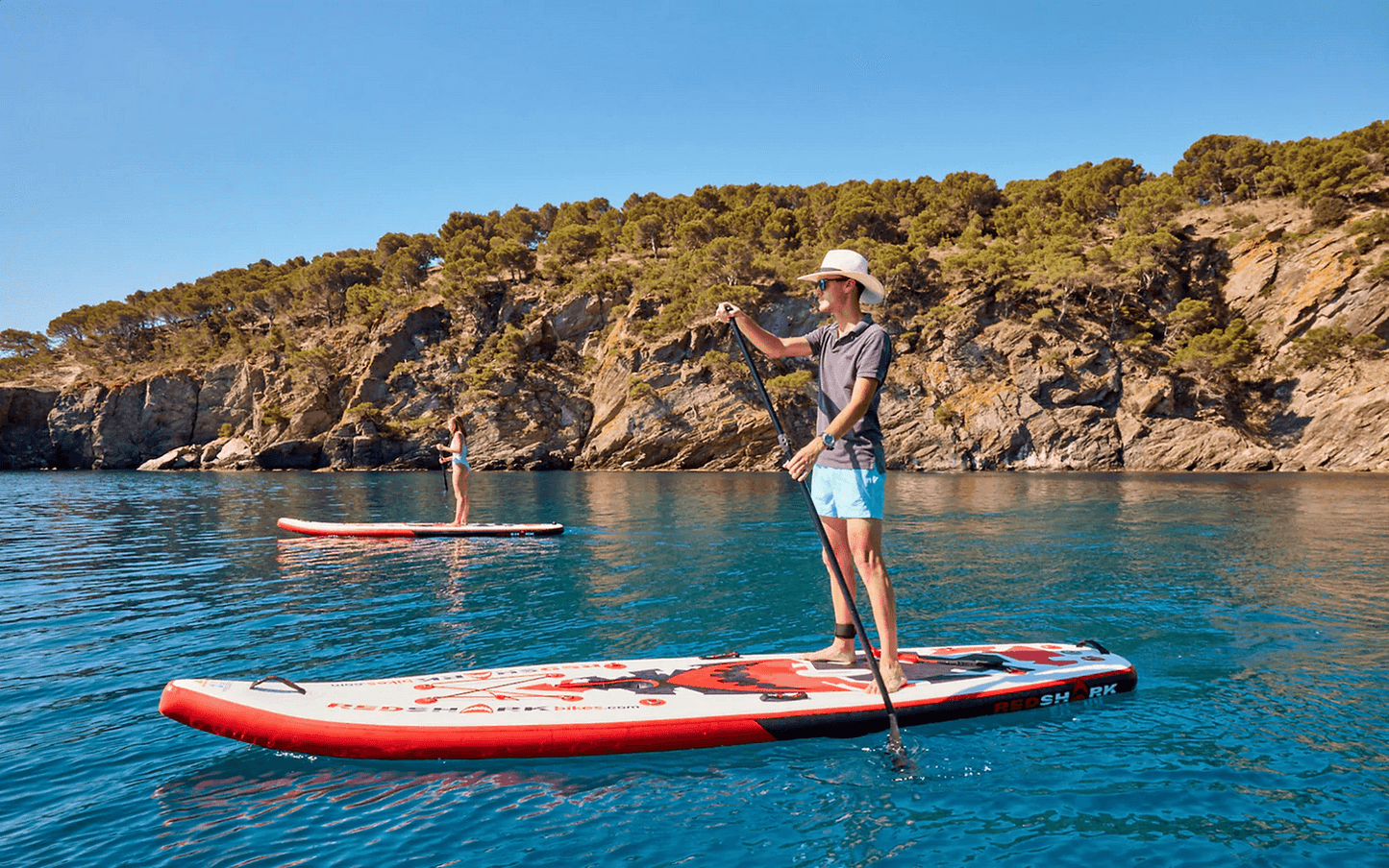 Person paddling a Red Shark water bike with adjustable SUP paddle kit and leash on a calm blue sea.